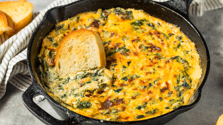 Pan of spinach dip, with a slice of toast sitting in it