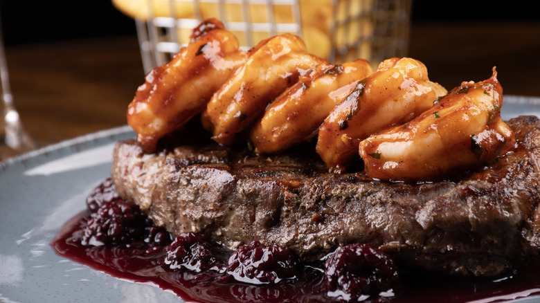 A steak topped with glazed shrimp