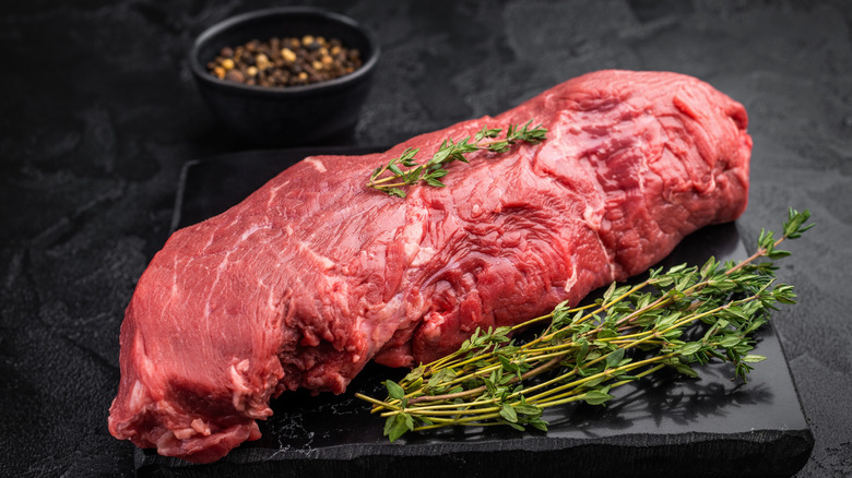 Raw beef tenderloin with black peppercorns and thyme sprigs