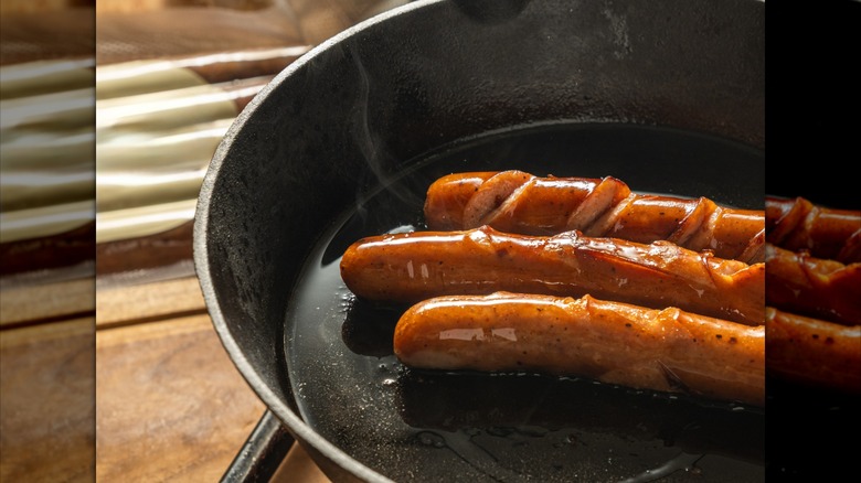 Hot dogs frying in a pan with bacon grease