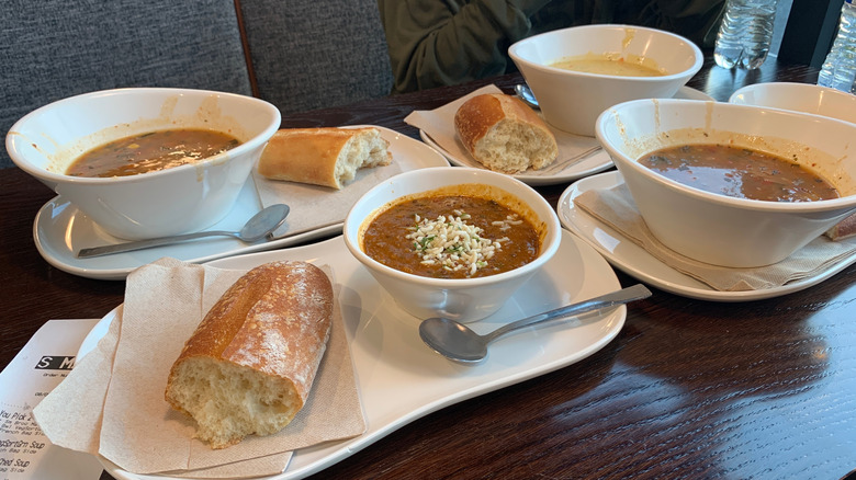 Four bowls of soup from Panera Bread on plates with bread