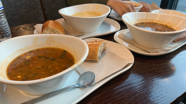 Three bowls of soup with bread on three individual plates