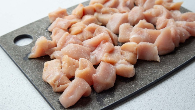 Raw chicken chunks on a gray board