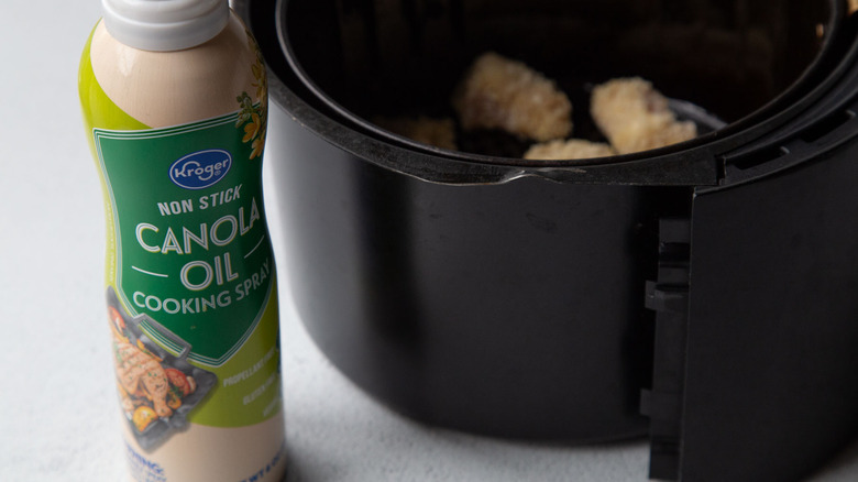 Breaded chicken chunks in an air fryer next to cooking spray