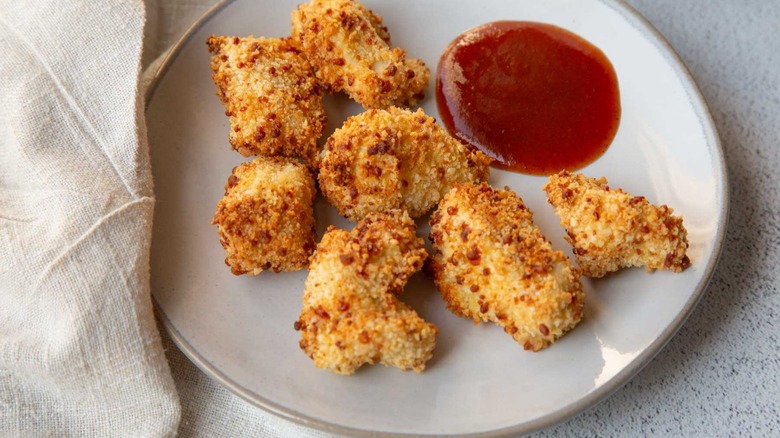 Popcorn chicken on a white plate with ketchup