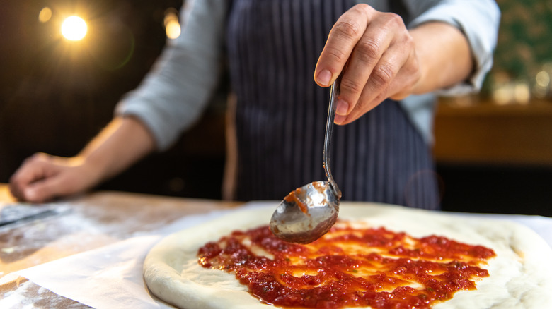 Chef applying sauce to pizza dough