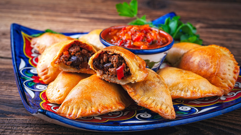 A plate of Argentinian empanadas, with one sliced open to show its meat filling.
