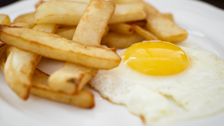 close up of a fried egg with fries on a white plate.