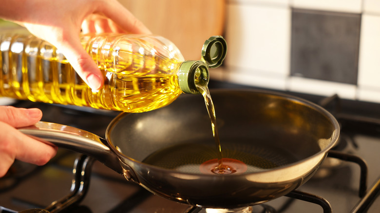 Person pouring cooking oil into pan