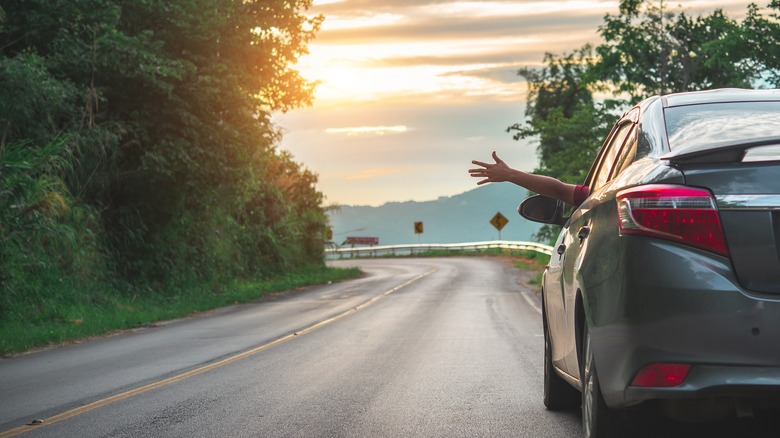 A car driving down the highway with a hand out the window.