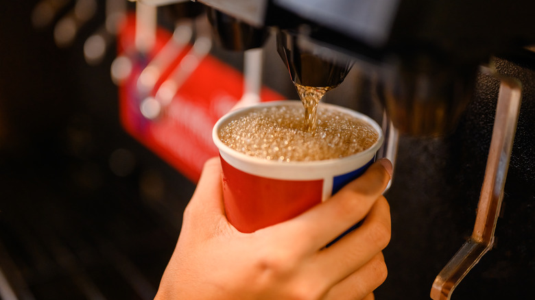 A person fills a plastic cup with soda