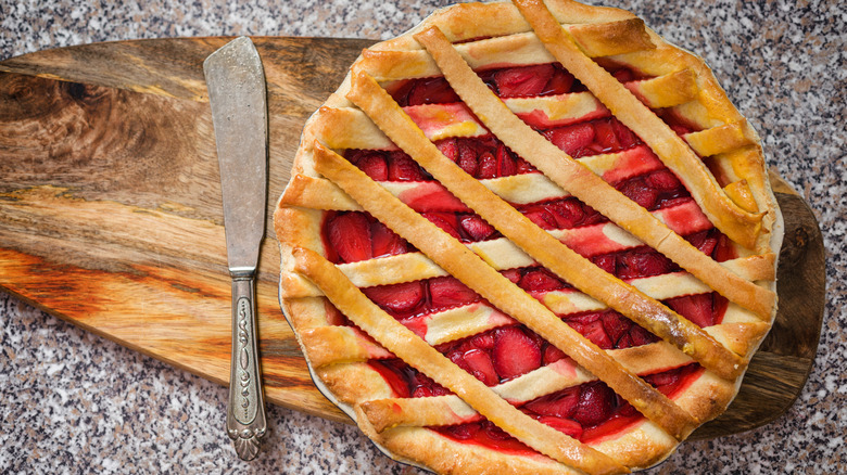 Strawberry pie with a lattice top on a wooden board next to a knife