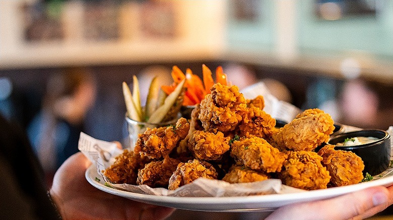 arms holding a platter of chicken wings with sauce