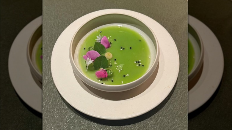 Bowl of green liquid with leaves, flower petals, sesame seeds