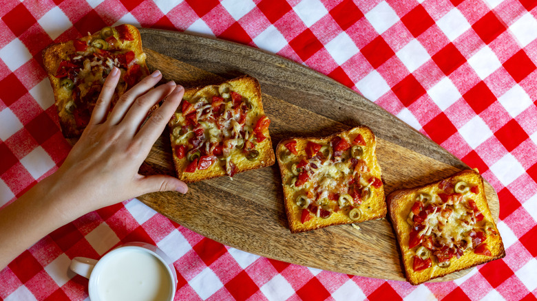 Hand reaching for pizza toast on oblong cutting board