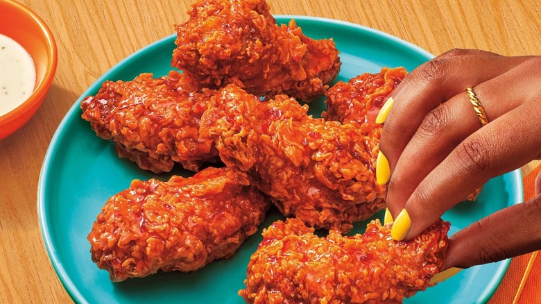 Hand holding Popeyes wings on a plate