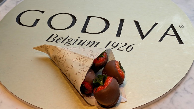 A wrapped bouquet of chocolate-covered strawberries next to a Godiva logo