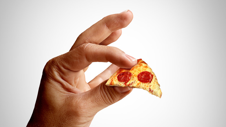 A hand holding a tiny slice of pizza, demonstrating shrinkflation