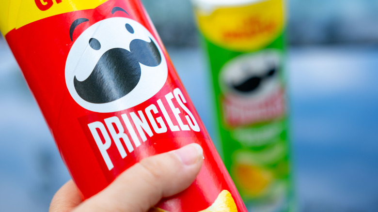 A hand holds a can of Pringles