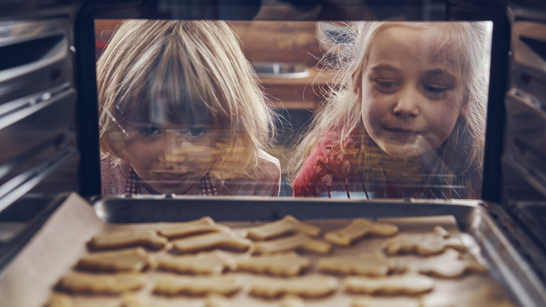 two children watching Christmas cookies bake