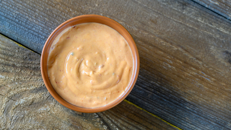 A bowl of creamy pink sauce sits on a wooden table