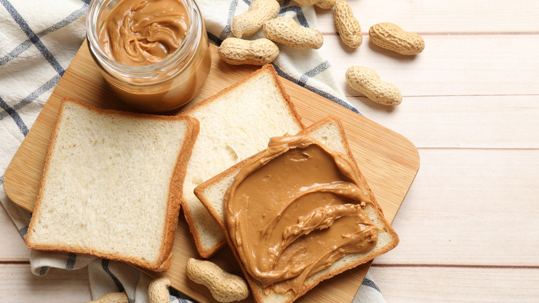 Peanut butter on bread with open jar and whole peanuts