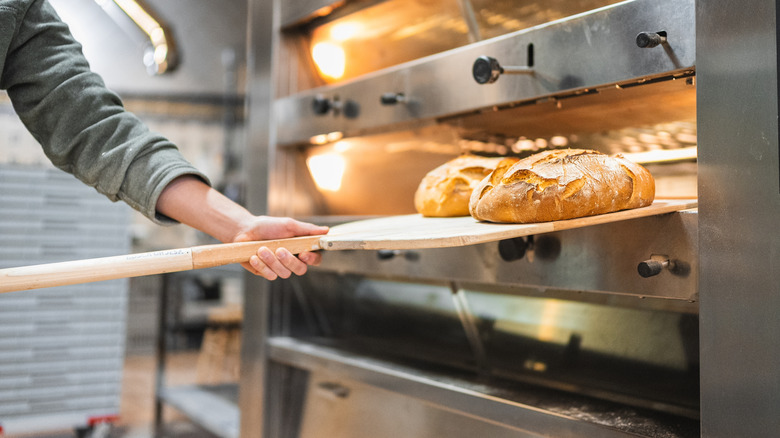 A baker is removing sourdough bread from a commercial oven.