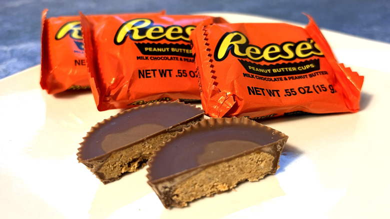 Reese's peanut butter cup sliced in half on a plate, in front of the product packages