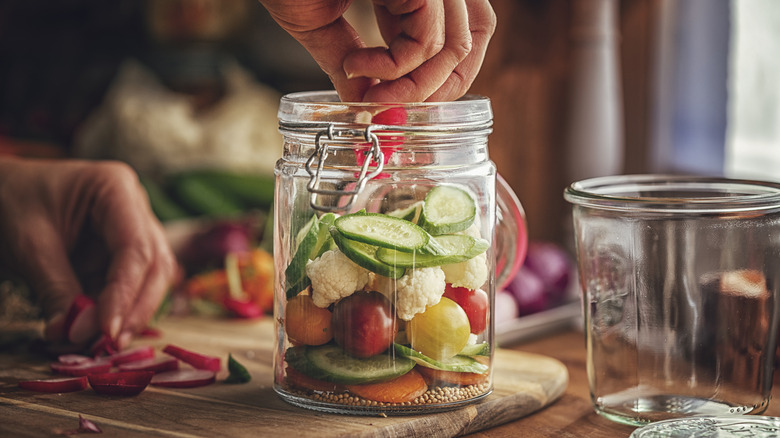 A person adding ingredients to a pickle jar
