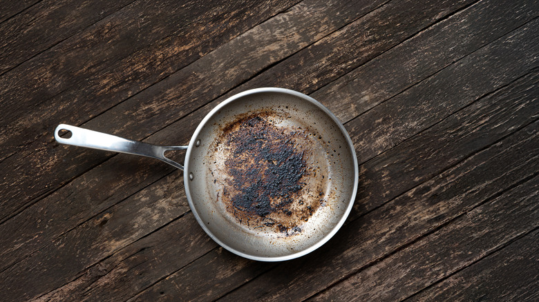 Dirty aluminum fry pan on a rustic wooden table.