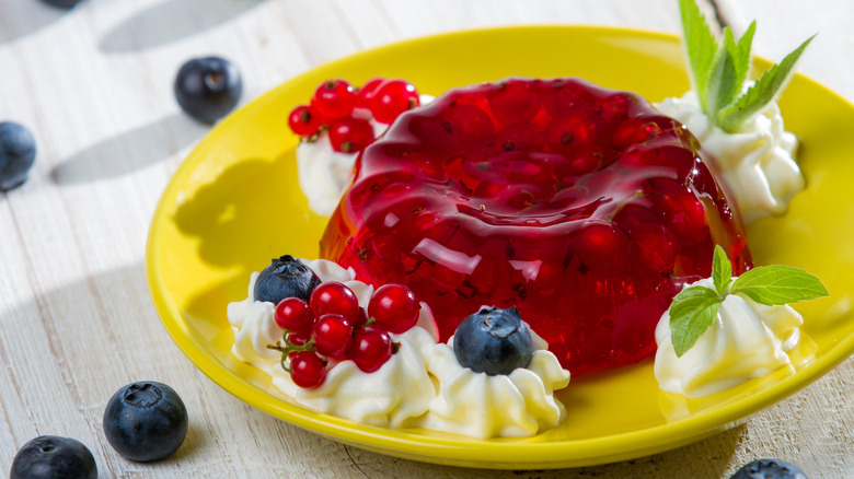 Cranberry jello salad with whipped cream, fruits, and mint leaves on a yellow plate