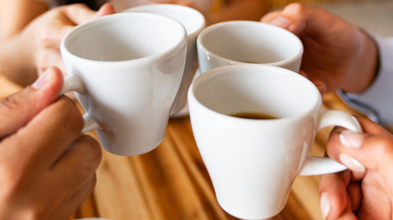 A group of people clink coffee mugs over a wooden table