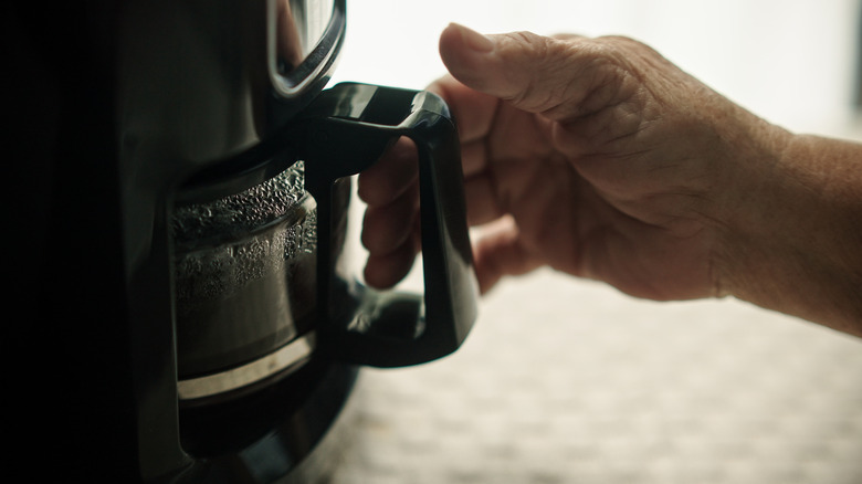 Close-up of a hand reaching for a glass pot of filter coffee