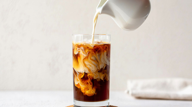A pitcher pouring milk into a glass of coffee