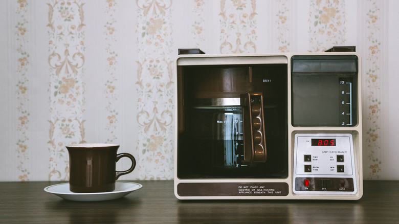 A retro coffee maker and mug posed on a wooden surface