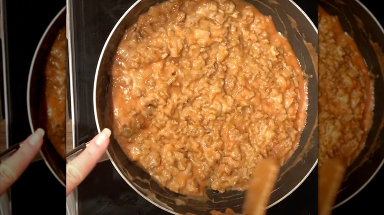 A hand and a spoon hover over a pot of Irish-Italian spaghetti meat sauce