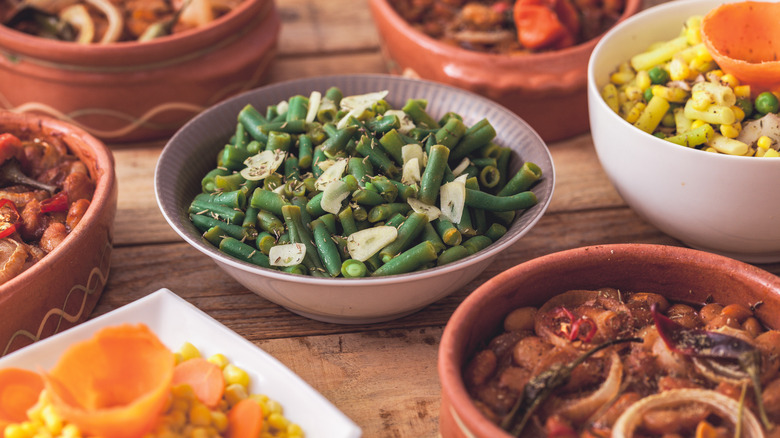 Green beans, bean salad, and other side dishes in bowls on wooden table