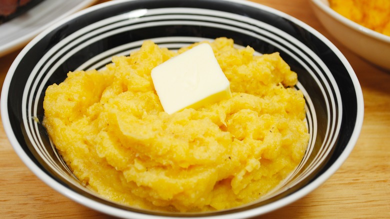 Mashed turnips with knob of butter in bowl on wooden table