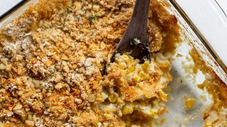 Scalloped corn in glass casserole dish with wooden spoon