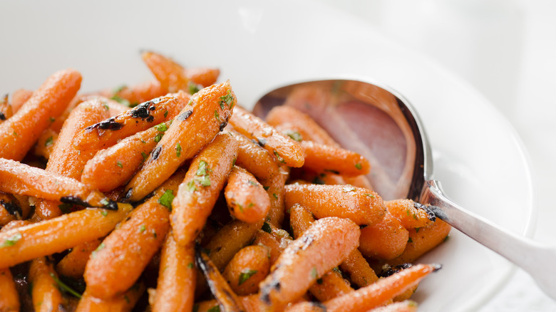A plate of candied baby carrots, with a serving spoon