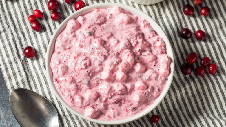 A bowl of pink cranberry fluff, surrounded by fresh cranberries