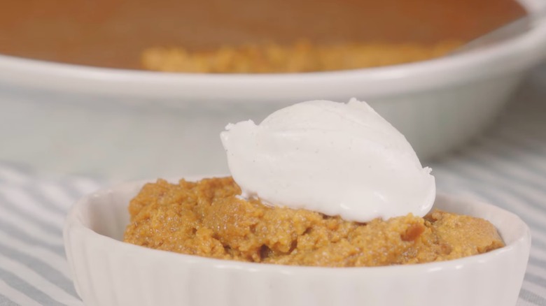 A piece of hasty pudding in a bowl, topped with whipped cream