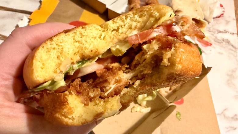 Hand holding a Bacon Caesar McCrispy Sandwich with a bite taken out