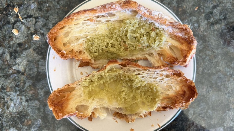 Opened croissant with green pistachio filling on a white plate on counter