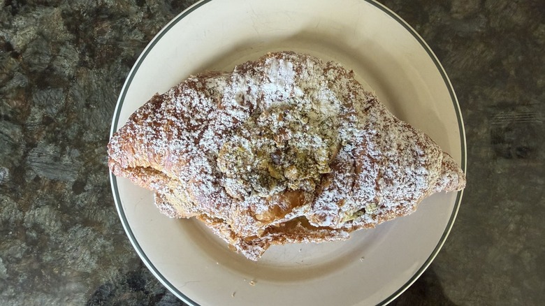 Croissant with powdered sugar and pistachio on white plate