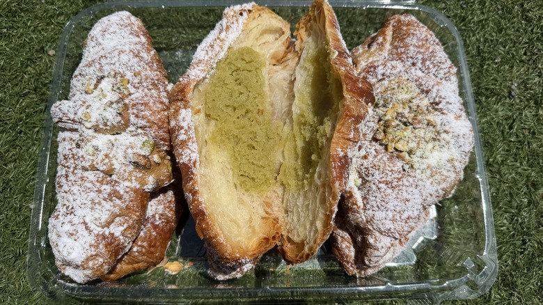 Pistachio croissants in open plastic container against grass background
