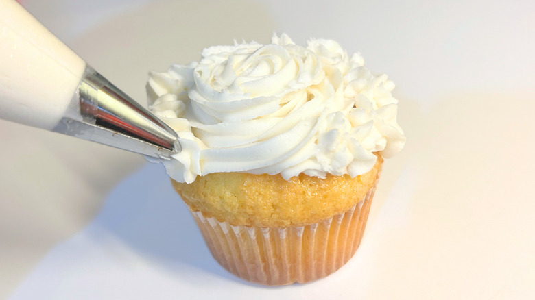 Close up of a piping bag piping white icing onto a cupcake