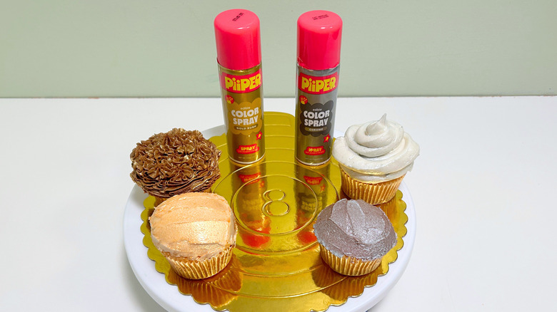 Two cans of PiiPER Color Spray with four decorated cupcakes