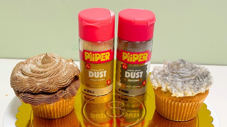 Two containers of PiiPER Edible Glitter Dust and two cupcakes on a metal cake stand