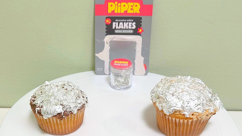 A container of PiiPER Decorative Edible Flakes in Real Silver and two cupcakes decorated with the silver flakes